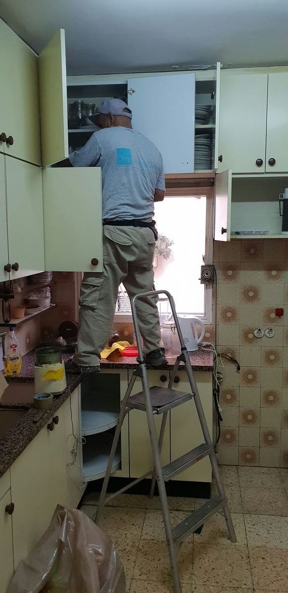 עובד עומד על סולם ומפנה את הארונות העליונים במטבח מסודר