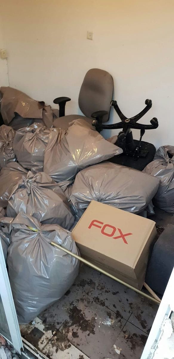 חדר עם שקיות פסולת אפורות רבות, כיסא משרדי וארגז קרטון, ולכלוך על הרצפה