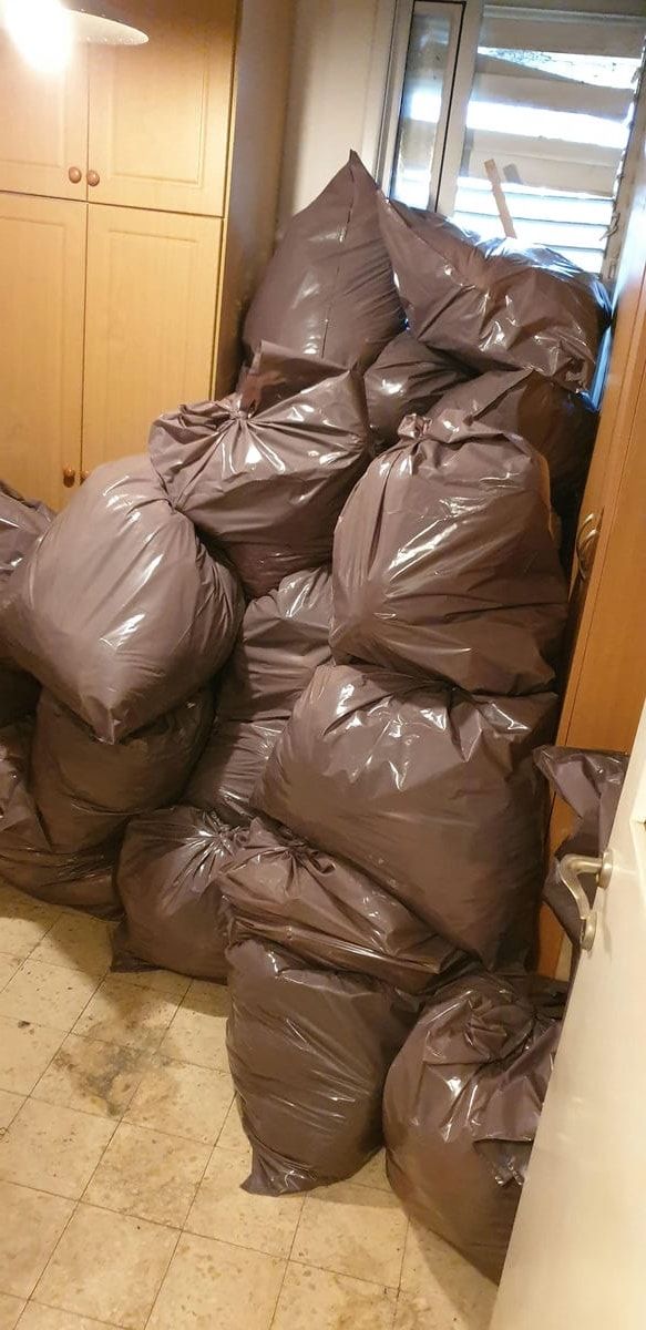 ערימה גבוהה של שקיות אשפה חומות מלאות בפינת חדר ליד ארון בגדים