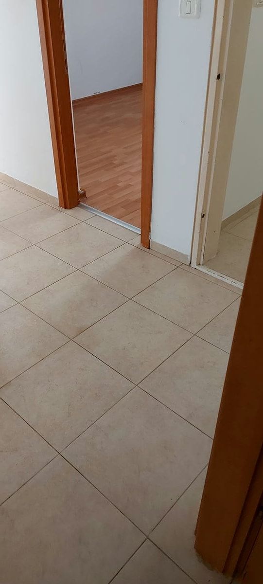 מסדרון ריק ונקי עם רצפת אריחים בהירה ודלת פתוחה לחדר ריק עם פרקט
