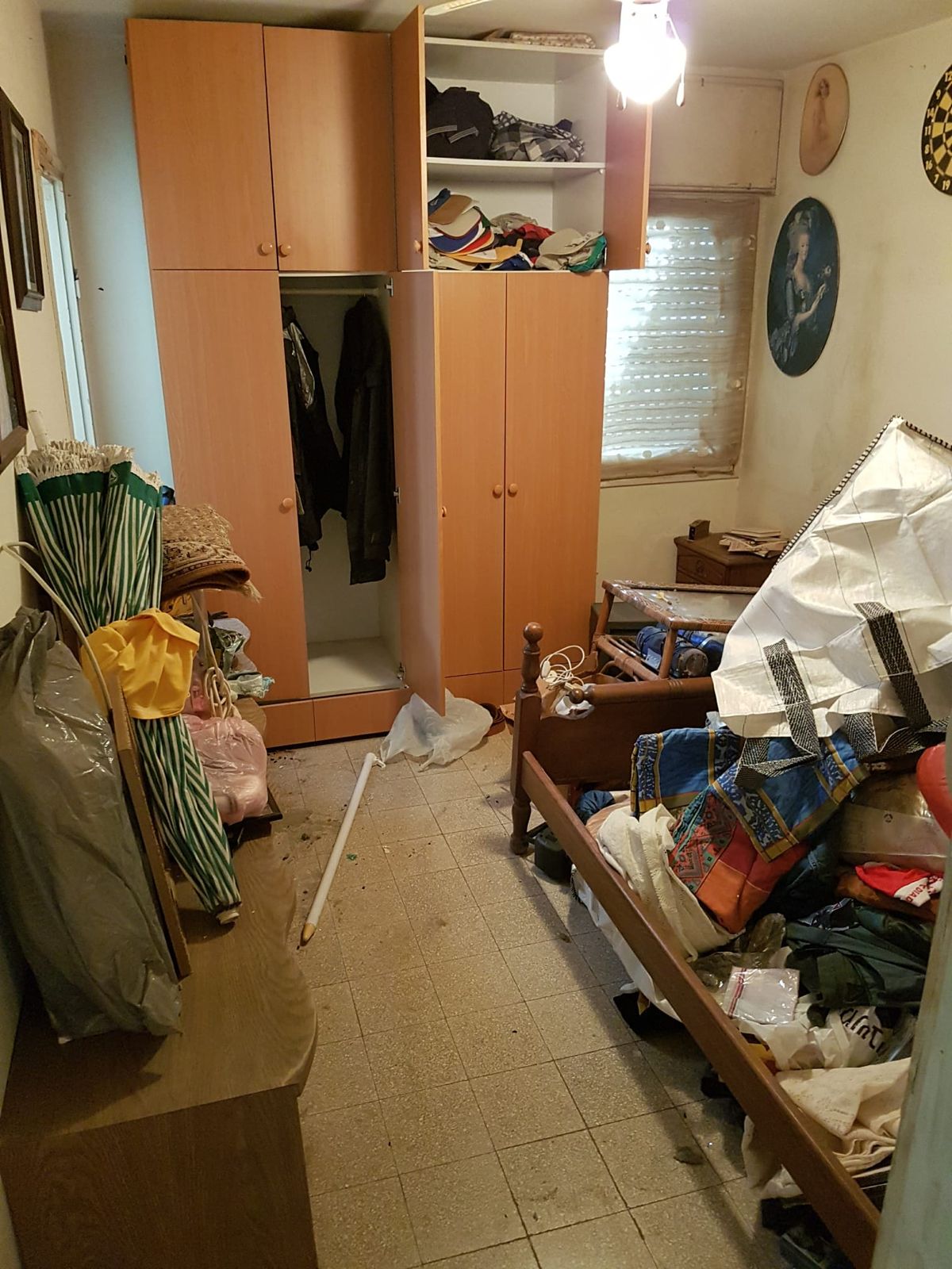 חדר שינה עם ארון בגדים פתוח, ומיטה ופינות החדר מכוסות בשקיות ובחפצים