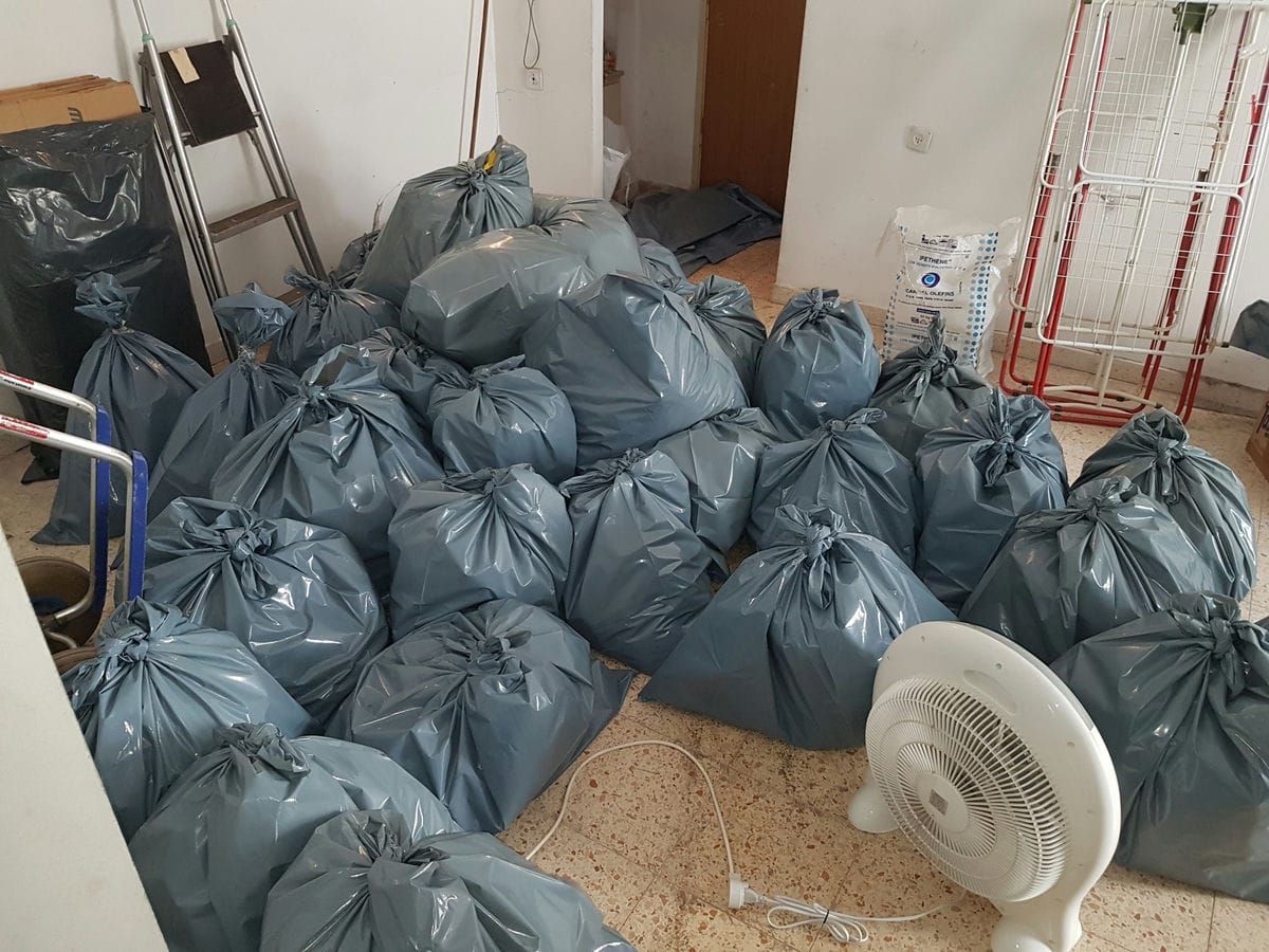 עשרות שקיות תכלת קשורות על רצפת חדר, לצד סולם, מאוורר ומתקן לייבוש כביסה