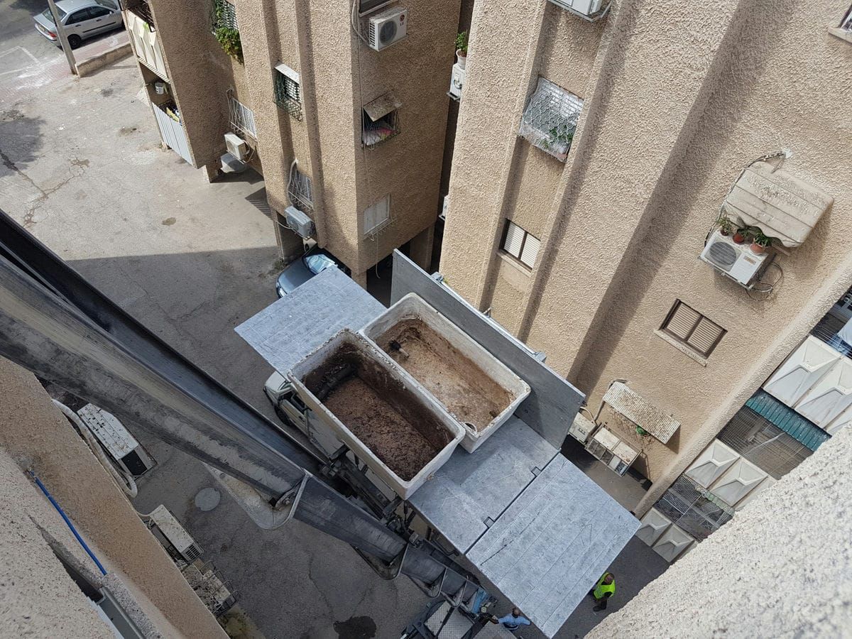 מבט מגובה על מנוף הרמה הנושא שתי אדניות עם אדמה בין בנייני מגורים