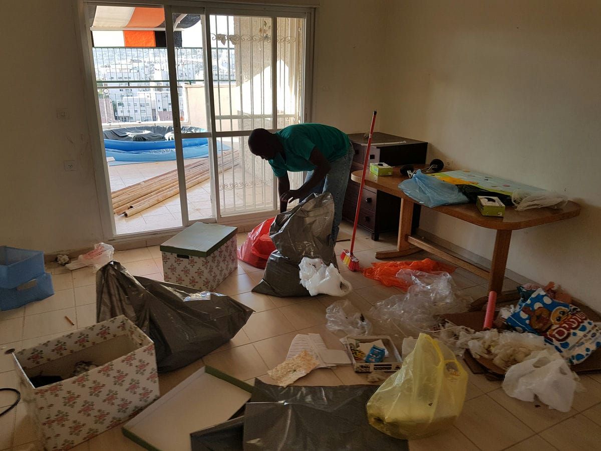 עובד ממלא שקית בסלון שהתרוקן חלקית, עם קרטונים ושקיות על הרצפה ויציאה למרפסת