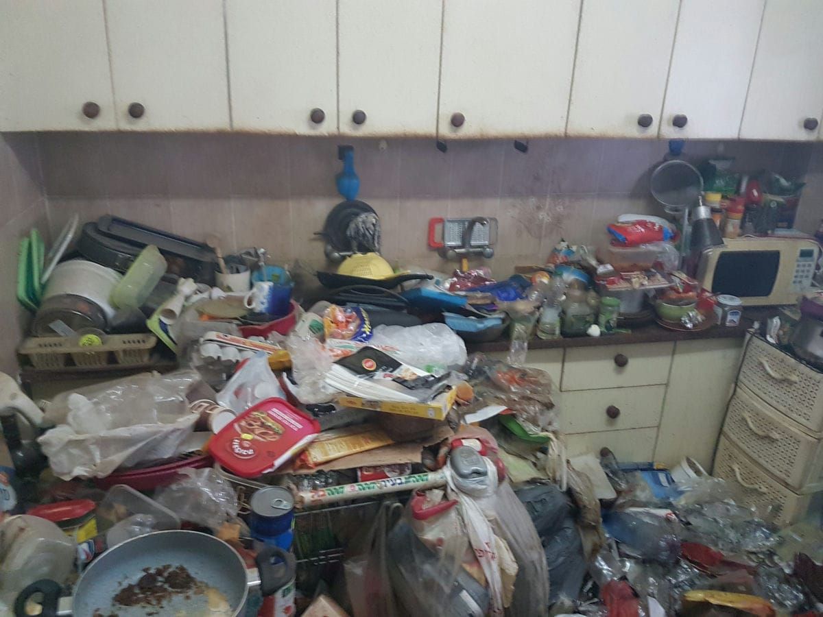 שיש מטבח עמוס בכלים, אריזות מזון, מחבתות ושקיות, מתחת לארונות לבנים