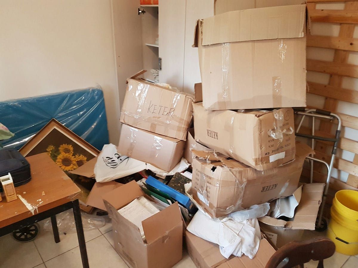 חדר עם ארגזי קרטון ערומים, תמונה ממוסגרת, שולחן והליכון בפינה
