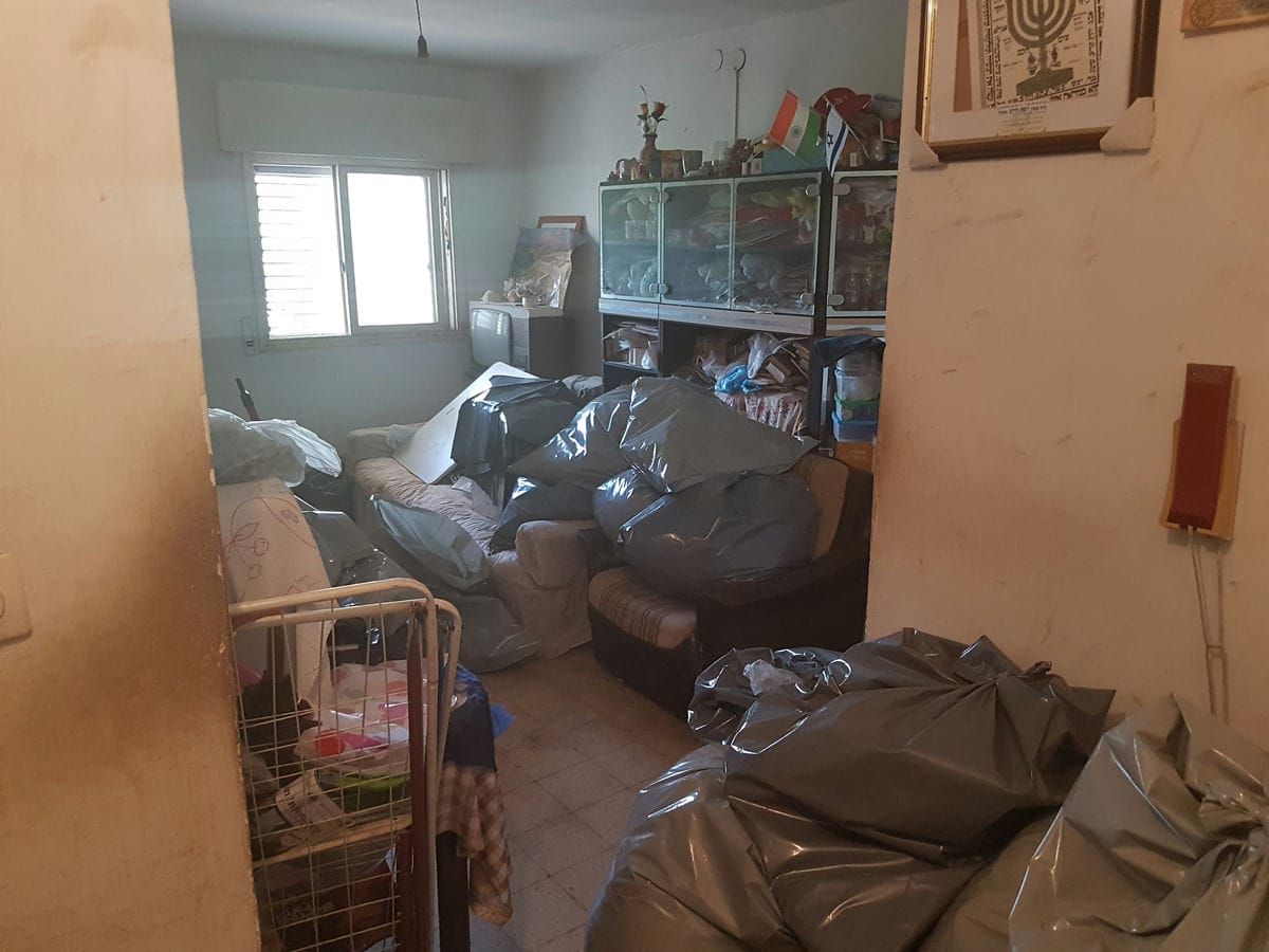 מבט ממסדרון לחדר מלא בשקיות פסולת גדולות, ספה וויטרינות זכוכית