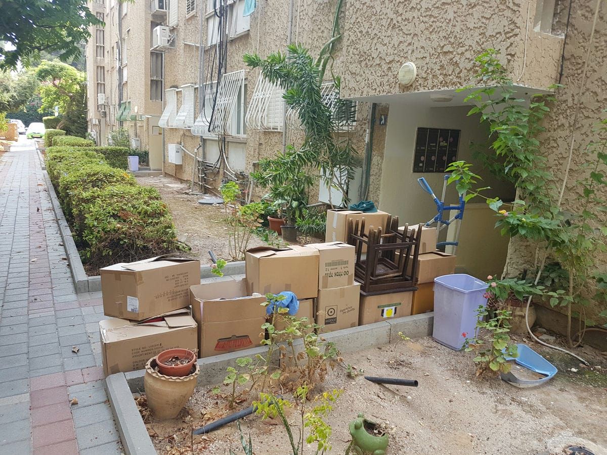 ארגזי קרטון וכיסאות ערומים בשביל הכניסה לבניין מגורים