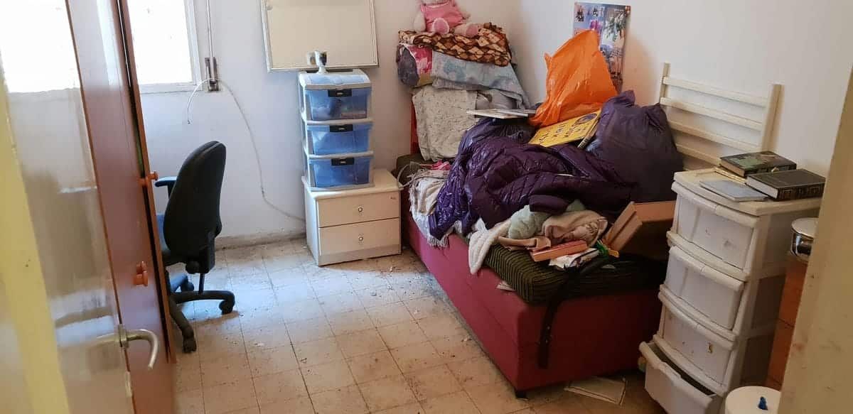 חדר שינה עמוס בבגדים וחפצים על מיטה לפני פינוי