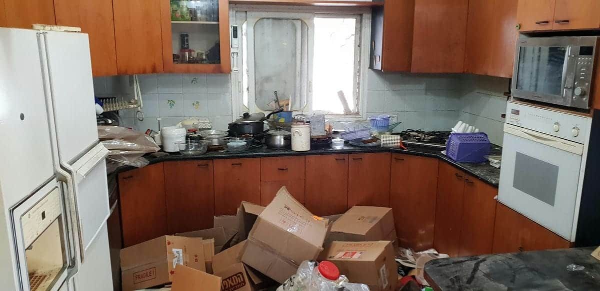 מטבח עם ארונות עץ, מקרר ותנור, וארגזי קרטון פתוחים רבים על הרצפה